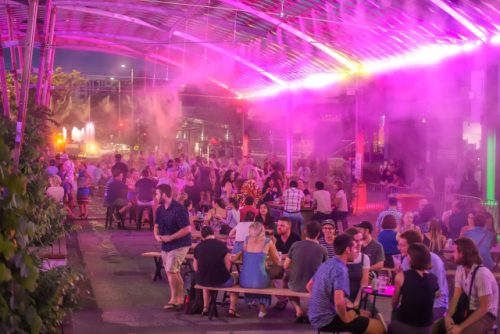 A group of people sit around tables at an outdoor event. 