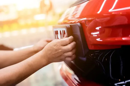 Hands removing a licence plate from the front of a red car