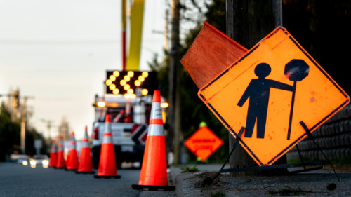 A yellow sign showing a black illustration of a traffic worker holding up a traffic management sign. 